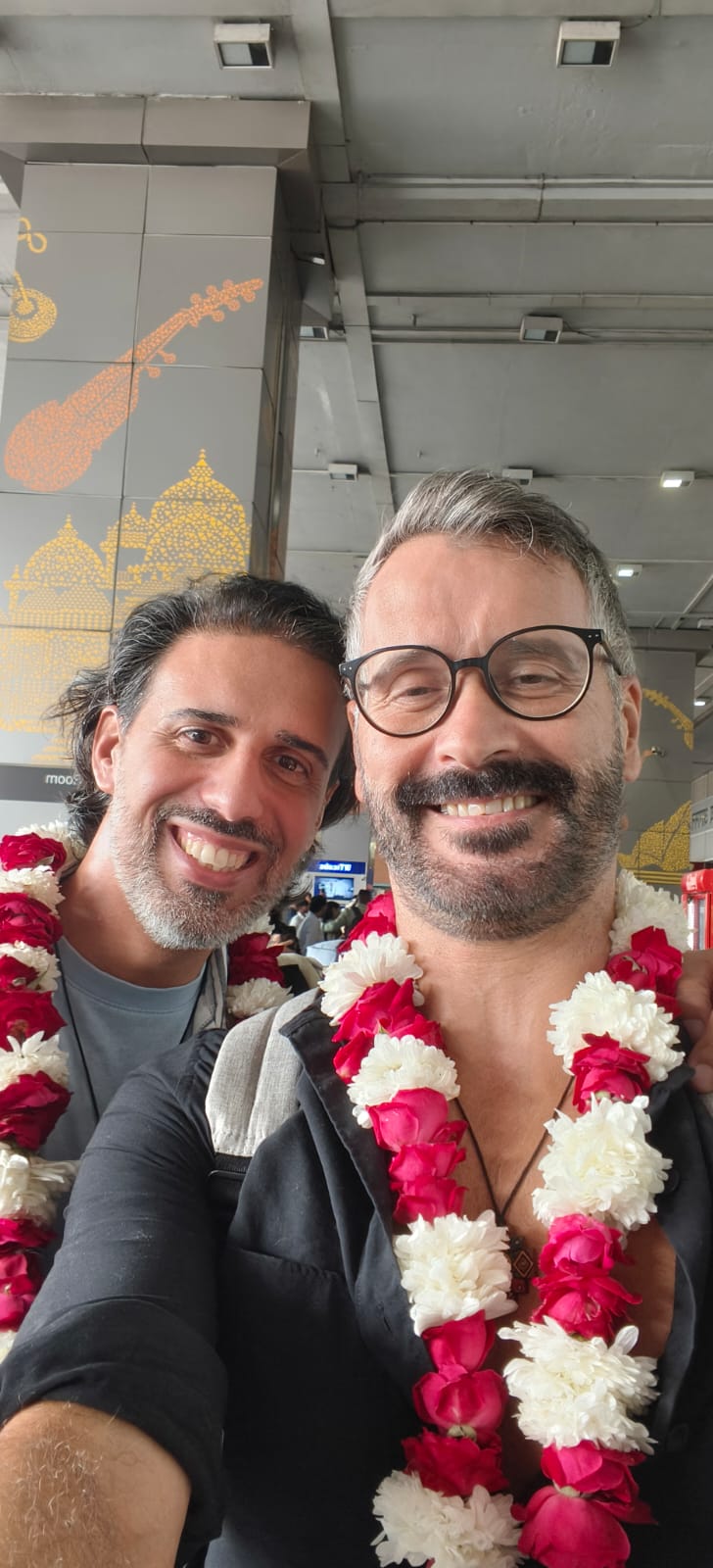 Two smiling travellers wearing red and white flower garlands at the airport