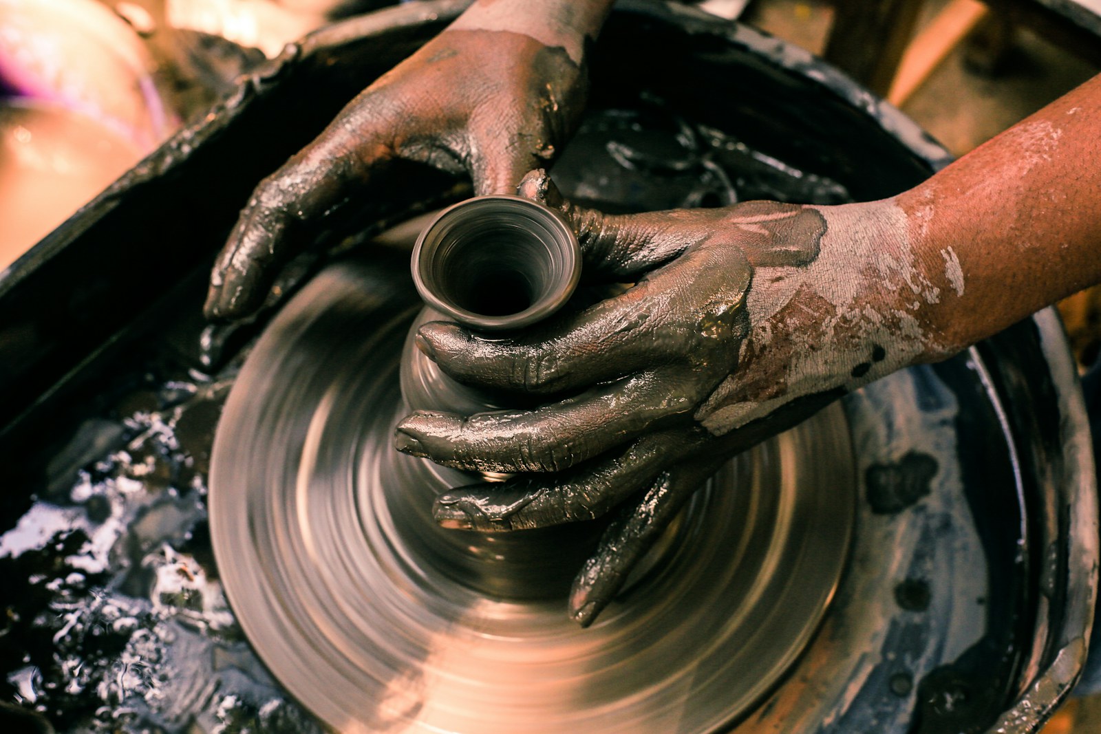 Hands shaping a clay pot on a spinning pottery wheel