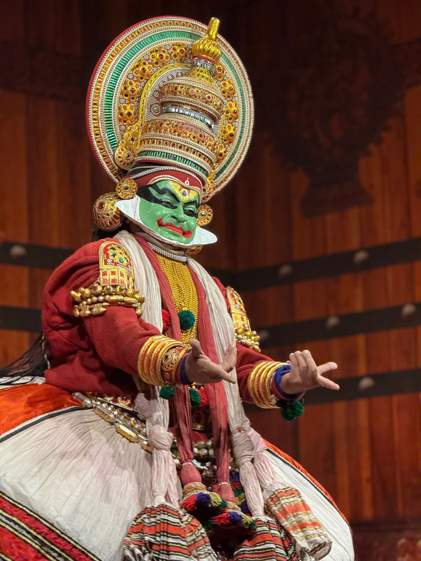 A Kathakali performer in an ornate headdress and red-and-white costume, making hand gestures.