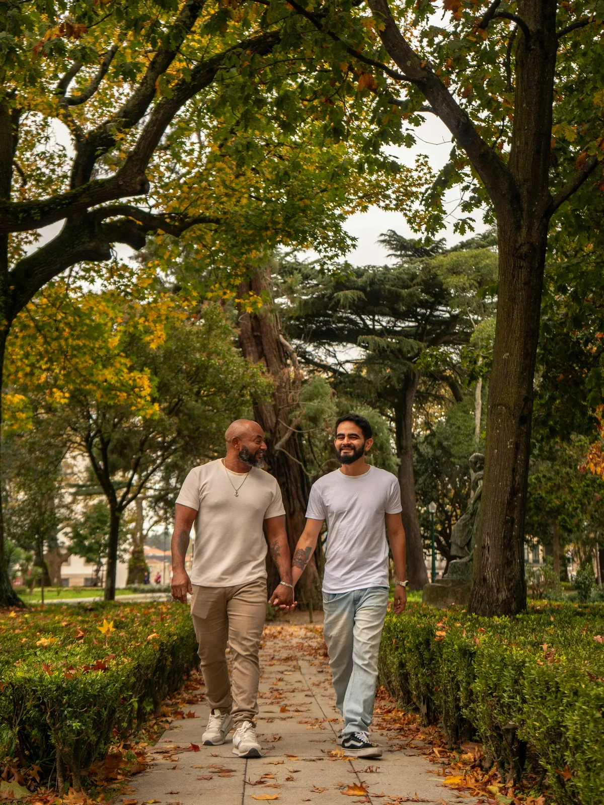A gay couple walking hand in hand through a leafy park