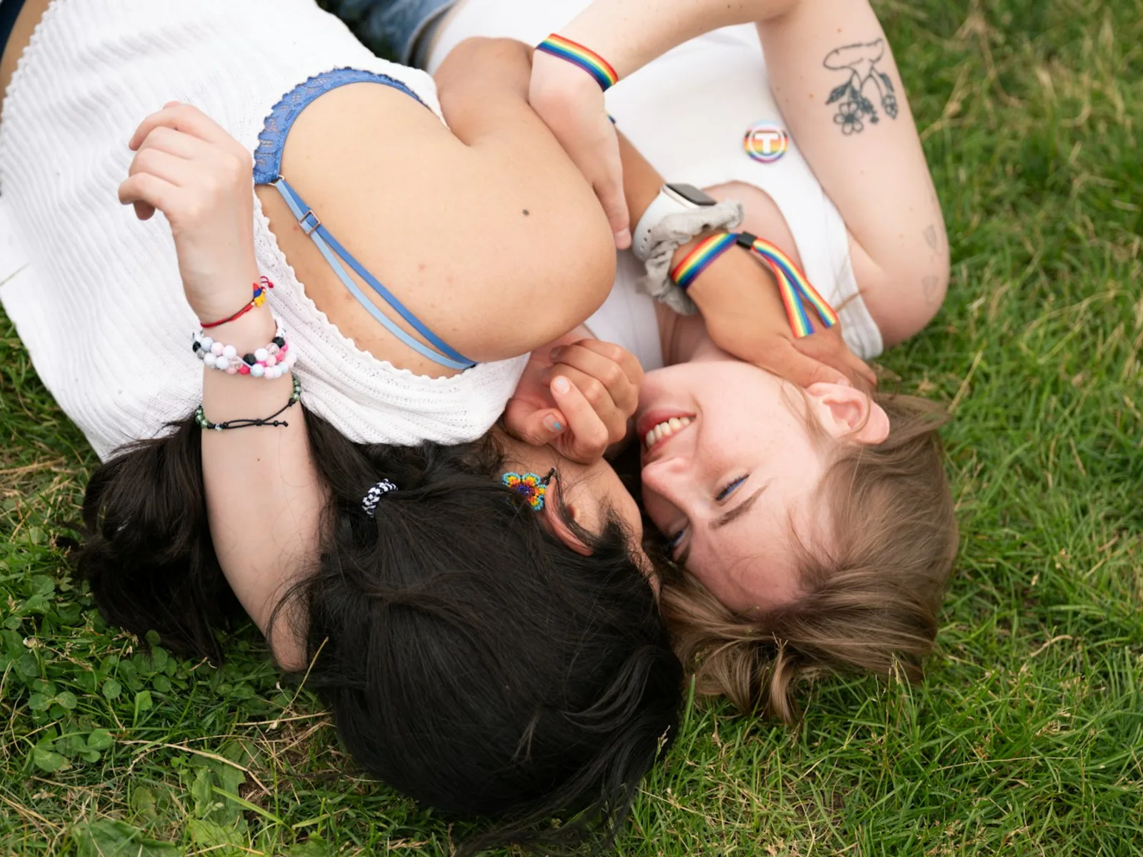Two women wearing Pride accessories smiling together on the grass